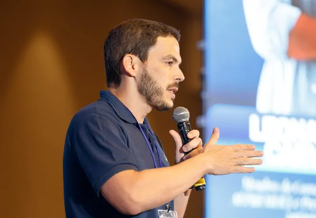Integrante da LEMA, de camisa polo da empresa, falando ao microfone no palco do Seminário de Investimentos AEPREMERJ.